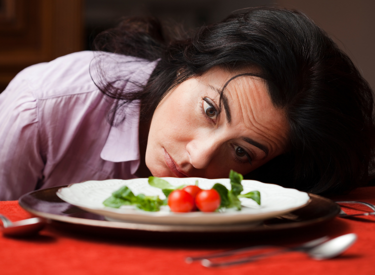 A woman staring at a plate with tomatoes